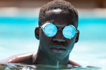 Calm African American male in stylish sunglasses with reflection of water swimming in pool against blurred background on sunny summer day — Stock Photo