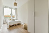 Комфортне ліжко з ковдрою та подушками, розташоване біля вікна в сонячній спальні сучасної квартири — стокове фото