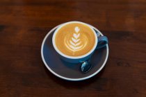 Зверху чашка гарячої кави з латте на тарілці з чайною ложкою, поданою на дерев'яному столі в легкому кафе — стокове фото