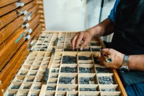 From above of crop concentrated senior male artisan in apron and eyeglasses choosing printing press letters from wooden box during work in traditional atelier — Stock Photo