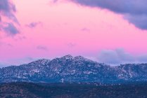 Impresionante paisaje de cordillera rocosa y valle con árboles verdes bajo el cielo rosado del atardecer con nubes en el Parque Nacional Sierra de Guadarrama en España - foto de stock
