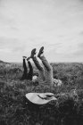 Preto e branco de vista lateral de amigos alegres em roupas casuais deitado com pernas levantadas no campo gramado na natureza à luz do dia — Fotografia de Stock