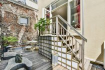 Escalera con barandilla metálica decorada con planta verde situada en terraza con sillas a la mesa cerca de casa moderna con ventana - foto de stock