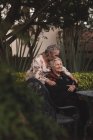 Счастливая пожилая женщина обнимает и целует сестру в голову, а затем улыбается, проводя время в саду вместе — стоковое фото