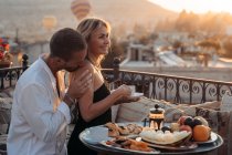 Вид сбоку любящего мужчины, целующего плечо жены во время совместного обеда и чаепития на террасе — стоковое фото