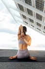 Full body of anonymous slim faceless female in activewear doing Gomukhasana with eagle arms while sitting near solar panel on street — Stock Photo