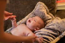 De cima de colheita mãe sem rosto segurando as mãos de bebê sem camisa adorável deitado em almofada macia no sofá em casa — Fotografia de Stock