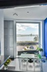 Modernes Esszimmerinterieur mit Stühlen und Tisch unter Lampe gegen Fensterwand und Wohnungstür — Stockfoto