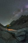Rückansicht eines unkenntlichen männlichen Touristen mit Fackel, der die schneebedeckten Berge bewundert, die sich nachts unter dem Sternenhimmel im Wasser spiegeln — Stockfoto