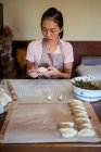 Donna in abiti casual e grembiule ripieno gnocchi con carne durante la preparazione tradizionale jiaozi cinese in cucina — Foto stock