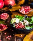 Appetizing pomegranate salad in bowl severed on wooden table with autumn leaves on black background — Stock Photo