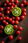 Vista superior de rodajas de bayas inmaduras de la planta de Solanum lycopersicum con tomates cherry dispersos - foto de stock