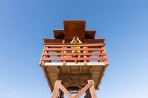 Angle bas de regarder à travers les jumelles sur la tour de guet en bois tout en surveillant la sécurité en mer contre le ciel bleu sans nuages — Photo de stock