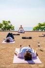 Yogalehrer in Aktivkleidung sitzt in Lotusposition, während Menschen bei sonnigem Wetter auf Matten auf dem Boden liegen, während Shavasana im Park stattfindet — Stockfoto