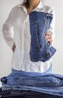 Crop anonimo femminile in camicia bianca con pila di jeans blu in mano — Foto stock