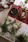 Vista superior do cenário de mesa de Natal com coroa na placa, ornamentos decorativos de madeira e toalha de mesa quadriculada vermelha com luzes amarelas no fundo — Fotografia de Stock