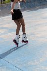 Cultivo anónimo piernas femeninas en patines blancos con ruedas rosas de pie sobre pavimento de hormigón en skate park - foto de stock