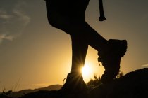 Silhouette des jambes d'une femme faisant du trekking dans la montagne avec le soleil créant une étoile de soleil avec son pied au coucher du soleil — Photo de stock