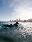Vista laterale della giovane surfista in muta sdraiata sull'acqua di mare ondulata e godendo della giornata estiva — Foto stock