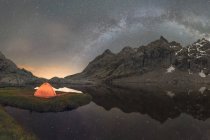 Vista panoramica della tenda sulla riva del lago contro la montagna innevata sotto cielo nuvoloso via lattea in serata situato nel Circo de Gredos cirque in Spagna — Foto stock