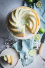 Vue de dessus du délicieux gâteau au citron vert servi sur une assiette blanche près des fleurs et des tranches de citron vert — Photo de stock
