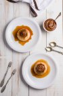 Top view of egg custards topped with sweet Dulce de leche served on white plates on table with cutlery in kitchen — Stock Photo