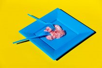 Montón de cerebros crudos rosados servidos en placa azul con tenedor de plástico sobre fondo amarillo en estudio creativo moderno y ligero - foto de stock