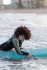 Side view of young happy female surfer in wetsuit lying on waving seawater and enjoying summer day — Stock Photo