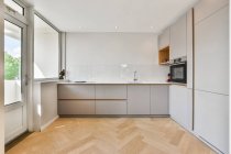 Творчий дизайн кухні з шафою і вбудована в піч проти вікна і дверей в будинку в сонячний день — стокове фото