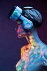 Женский манекен с VR гарнитурой, стоящий под ярким разноцветным освещением на фиолетовом фоне — стоковое фото