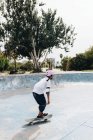 Повне тіло молодої етнічної людини в повсякденному вбранні в захисному шоломі з колінними подушечками і ліктями катання на скейтборді в скейтборді парку — стокове фото