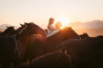 Щаслива жінка, яка милується заходом сонця над горами, виховуючись люблячою людиною серед спокійних коней у Туреччині. — стокове фото