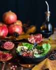 Appetizing pomegranate salad in bowl severed on wooden table with autumn leaves and bottle of olive oil on black background — Stock Photo