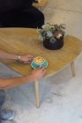 Crop pessoa anônima colocando caneca de café quente com arte latte em mesa de madeira com flores decorativas em casa de café — Fotografia de Stock