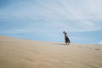 Повний вид на тіло босоніж у сукні, що йде по піщаній дюні в пустелі — стокове фото