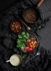 Top view of stewpan with lentils near salad with pumpkin and bell pepper decorated with green basil leaves on black background near salad dressing — Stock Photo