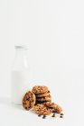 Haufen süßer knuspriger Kekse mit Schokoladenchips auf dem Tisch mit Krümeln und Milch auf weißem Hintergrund im Zimmer — Stockfoto