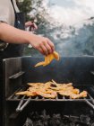 Анонимный шеф-повар выращивает сырую куриную крылышко на решетке из горячего металла с дымом во время пикника в сельской местности — стоковое фото