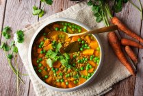 Schüssel mit köstlichem Carry Mahlzeit mit Gemüse garniert mit grünem Basilikum Blätter serviert in der Nähe Topf auf dem Tisch mit rohen Karotten — Stockfoto