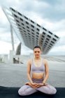 Full body of peaceful female in activewear with closed eyes practicing Padmasana posture on street against modern solar panel in city — Stock Photo