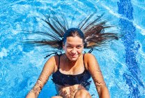 Зверху чарівна молода жінка в бікіні плаває в басейні з чистою водою, дивлячись на камеру влітку — стокове фото