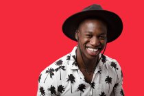 Positive masculine self-confident African American male in stylish outfit standing against red background and looking at camera — Stock Photo