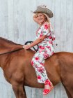 Side view full body of smiling senior female in cowboy hat holding rein on chestnut stallion — Stock Photo