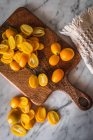 Pila vista dall'alto di kumquat freschi tagliati all'arancia su tagliere di legno posto sul tavolo di marmo con asciugamano in cucina — Foto stock