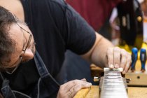 Crop männlicher Geigenbauer in Arbeitskleidung und Brille, der weiße Nuss am Gitarrenhals justiert, während er in einer professionellen Werkstatt mit Ausrüstung arbeitet — Stockfoto