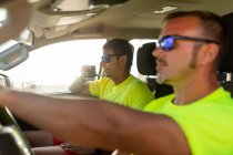 Seitenansicht des Rettungsschwimmers mit Sonnenbrille am Steuer eines Autos in der Nähe eines Mannes, der am Arbeitstag über ein Funkgerät spricht — Stockfoto