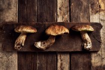 Вид сверху сырых грибов Boletus edulis на ржавой деревянной разделочной доске во время приготовления — стоковое фото