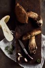 Draufsicht auf roh geschnittene Steinpilze auf hölzernem Schneidebrett mit Knoblauch und Petersilie in leichter Küche während des Kochvorgangs — Stockfoto