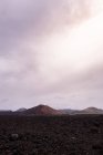 Ruta áspera entre lava oscura contra el volcán Bermeja en Yaiza, Lanzarote, Islas Canarias en España - foto de stock