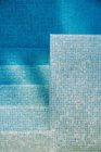 Вид сверху на плиточное дно и ступеньки в бассейне с чистой голубой водой — стоковое фото